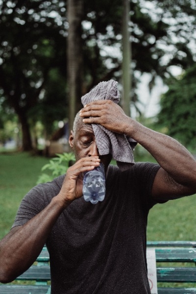 Guy outside wiping sweat off his forehead and drinking water